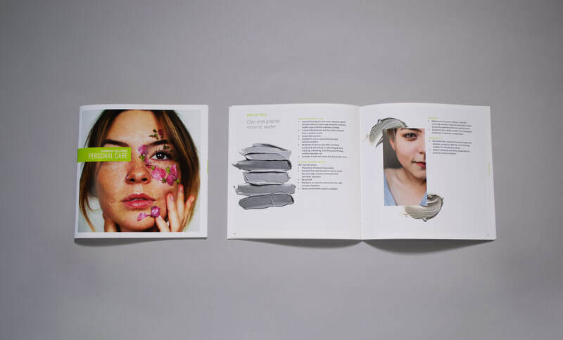 Photo of brochure cover with an open brochure beside it. The cover features a woman touching her face, which is covered in flower petals. Overlaid, there are chemical formulas. On the inside spread, there are images of swatches of clay as well imagery of a closeup of a person's face, cropped close to only show the right half of their face. They have a soft smile. The ingredients featured on this spread are natural ingredients such as clay.