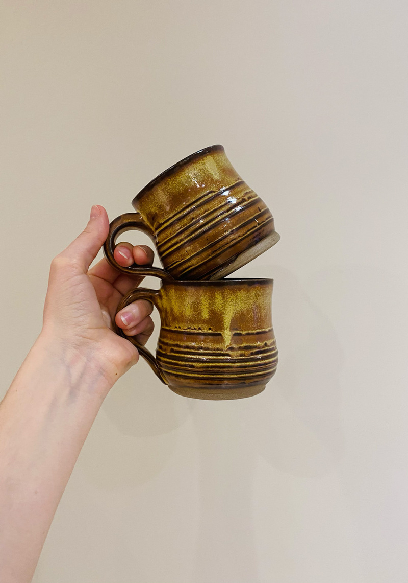 Two rustic yellow and rust brown mugs with horizontal striped texture.